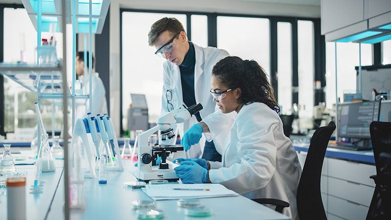 Two scientists in white coats working at a microscope