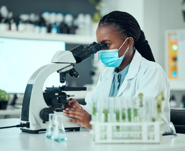 A lab technician in a mask and coat looking through a microscope